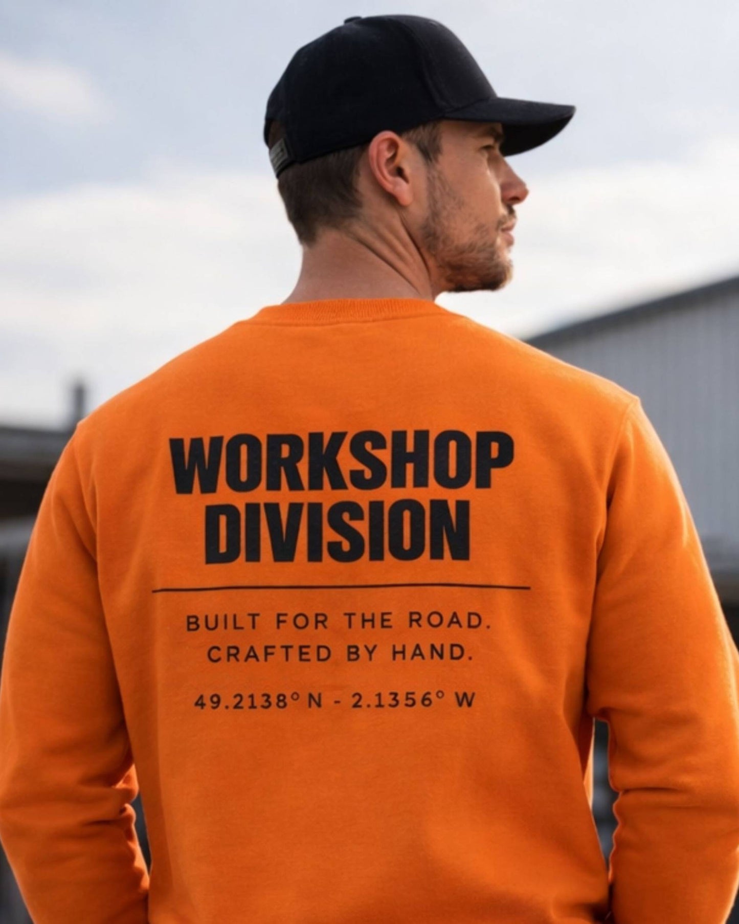 Man wearing an orange sweatshirt with 'Workshop Division' text, standing outdoors.