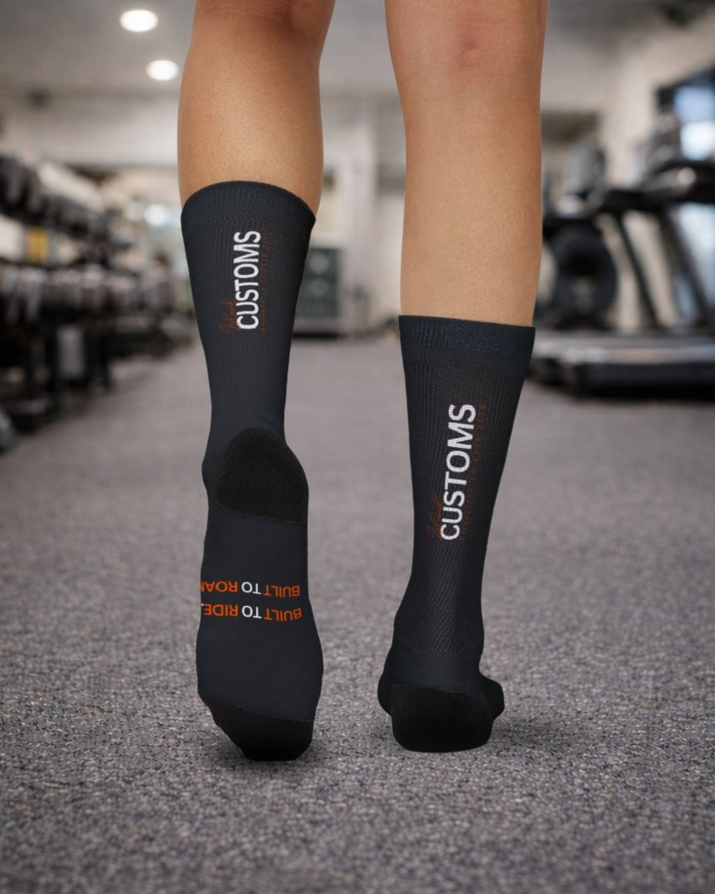 Black socks with 'CUSTOMS' branding worn by a person in a gym setting