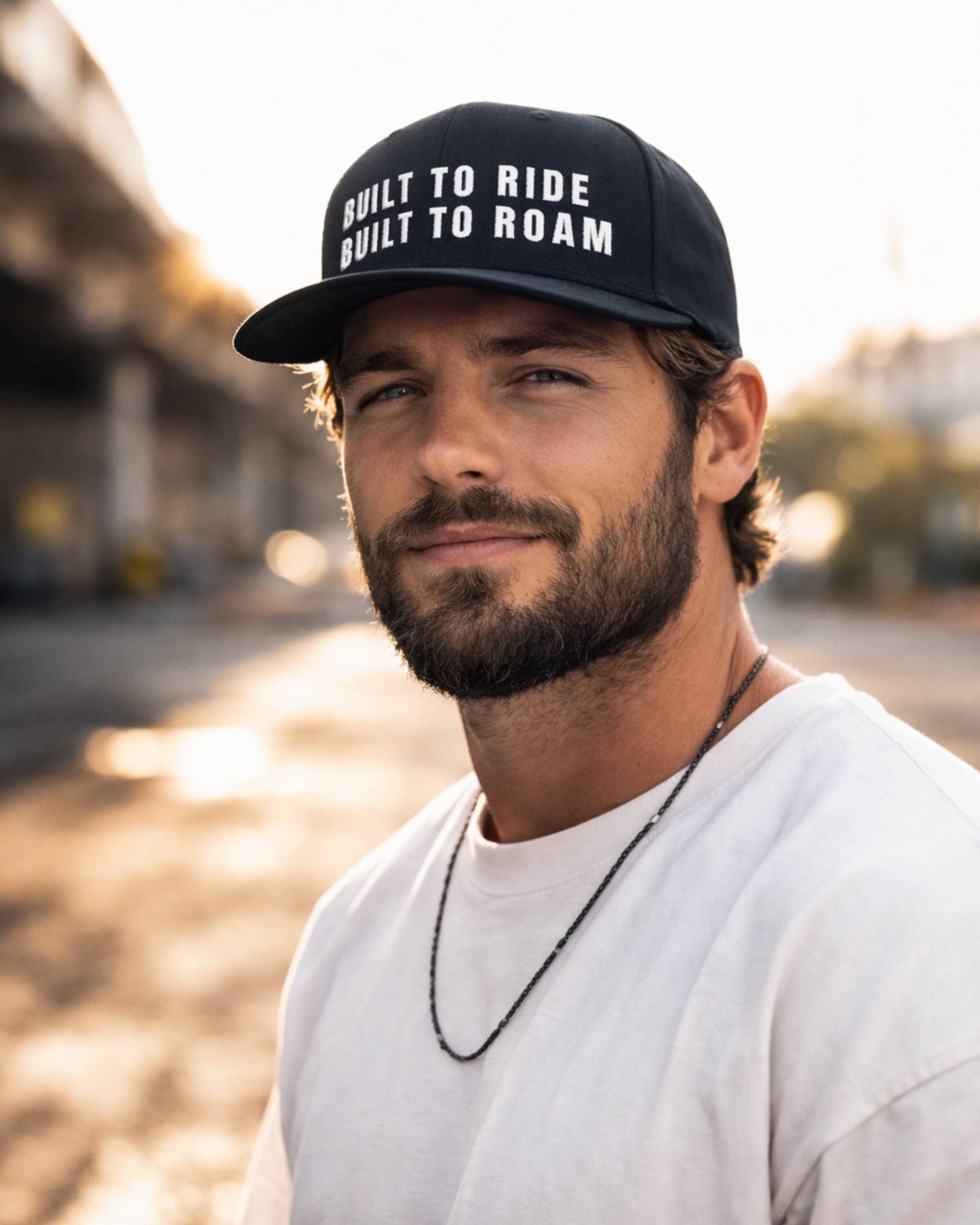 Man wearing a cap with 'Built to Ride, Built to Roam' text on a blurred street background