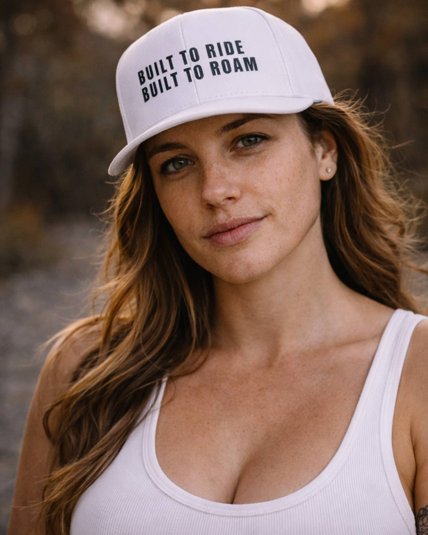 Woman wearing a white cap with text, standing outdoors.