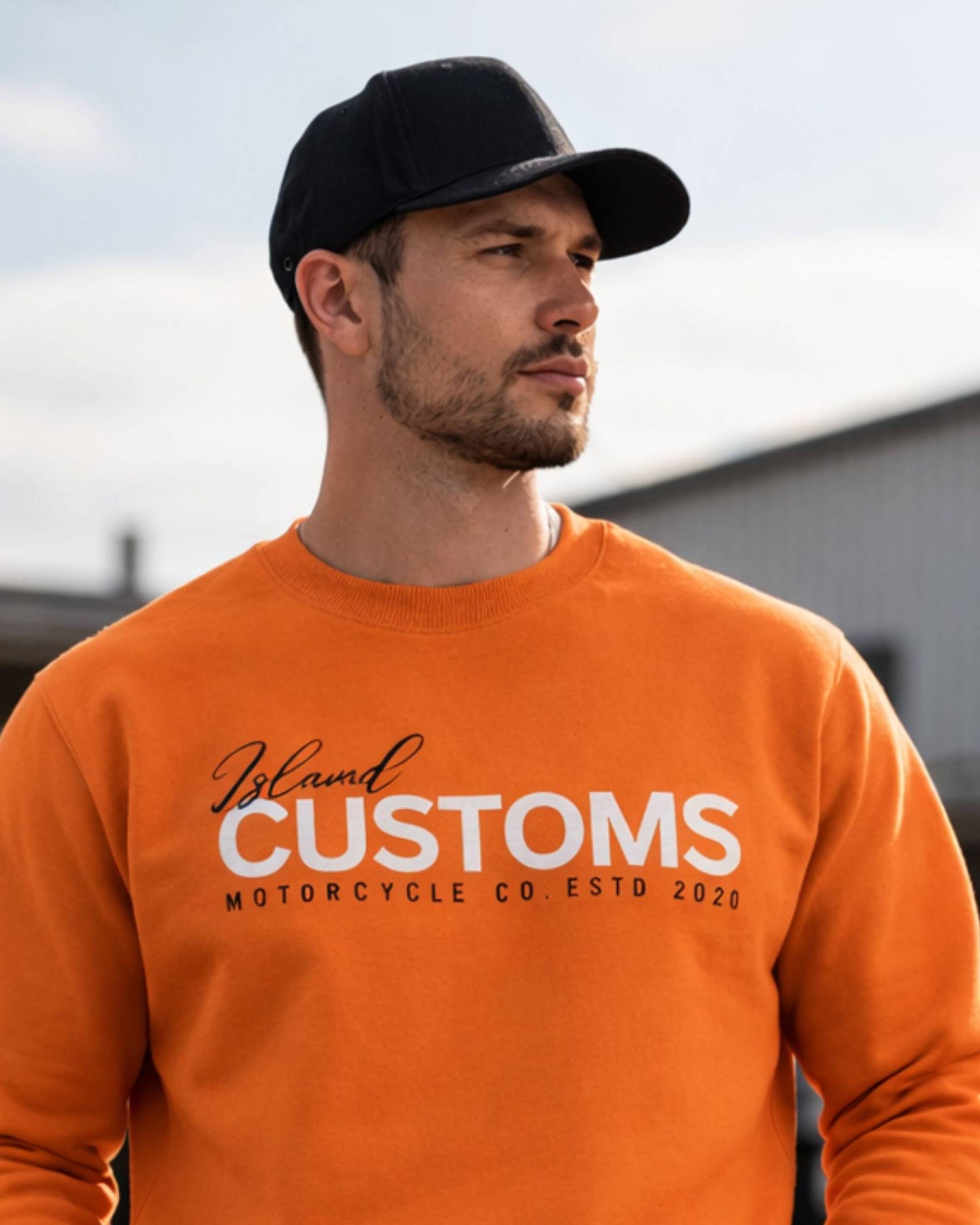 Man wearing an orange sweatshirt with 'Iceland Customs' text, standing outdoors.