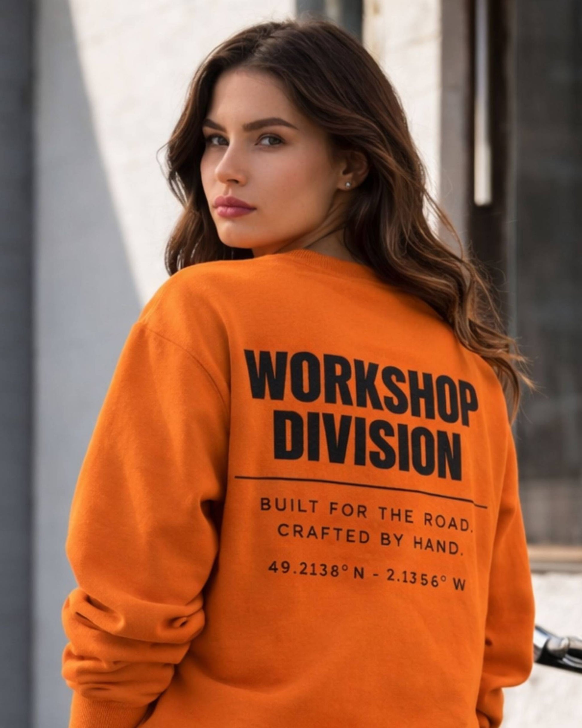 Woman wearing an orange sweatshirt with 'Workshop Division' text on the back.