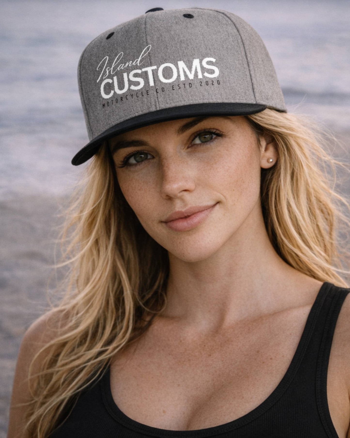 Woman wearing a gray cap with 'Island Customs' logo against a water background