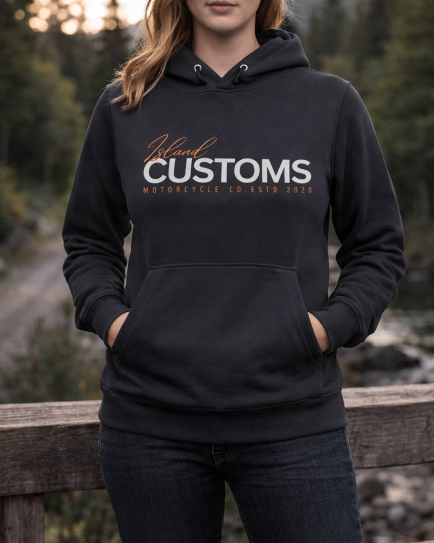 Person wearing a black hoodie with 'Island Customs' logo in a forest setting