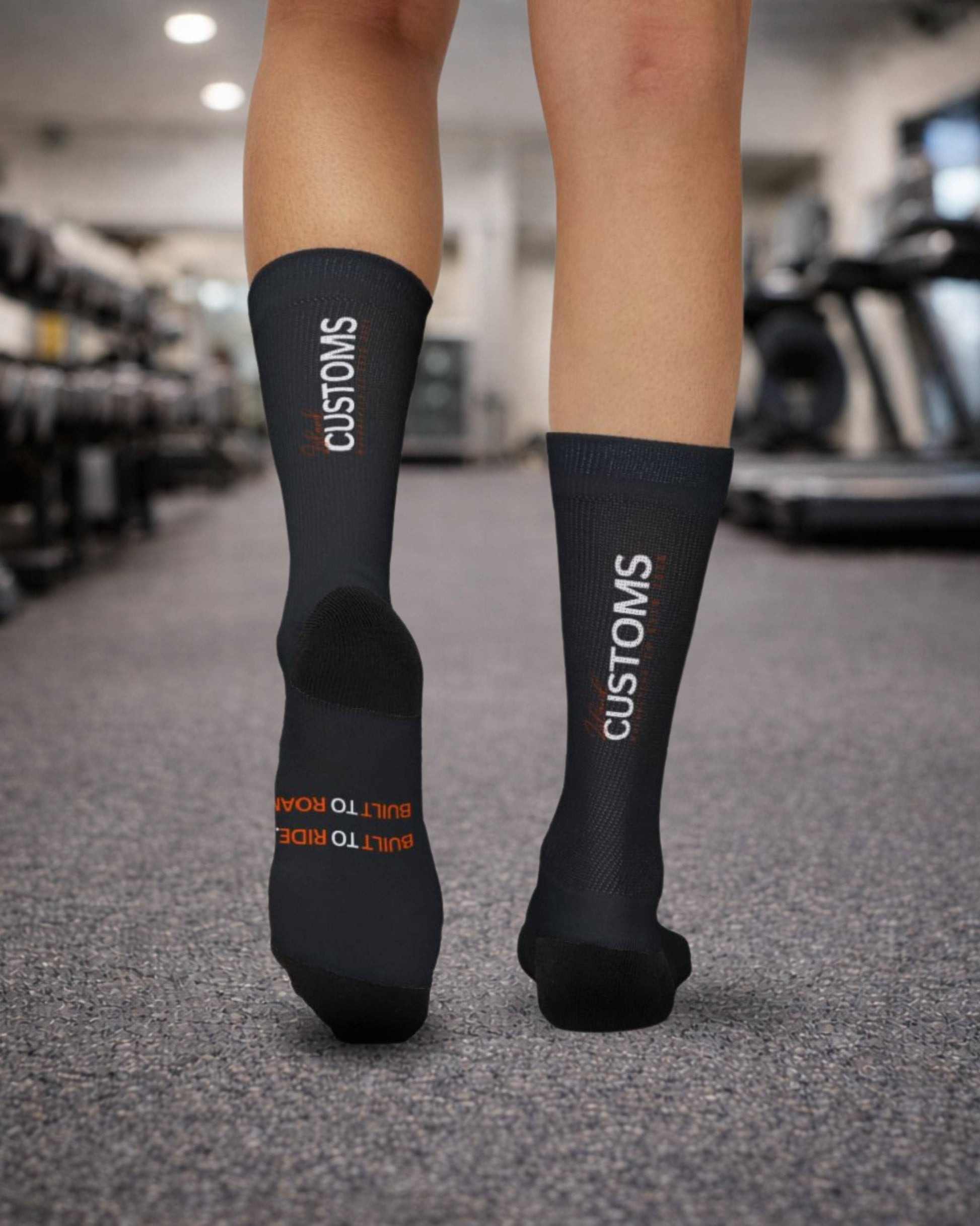 Black socks with 'CUSTOMS' branding worn by a person in a gym setting