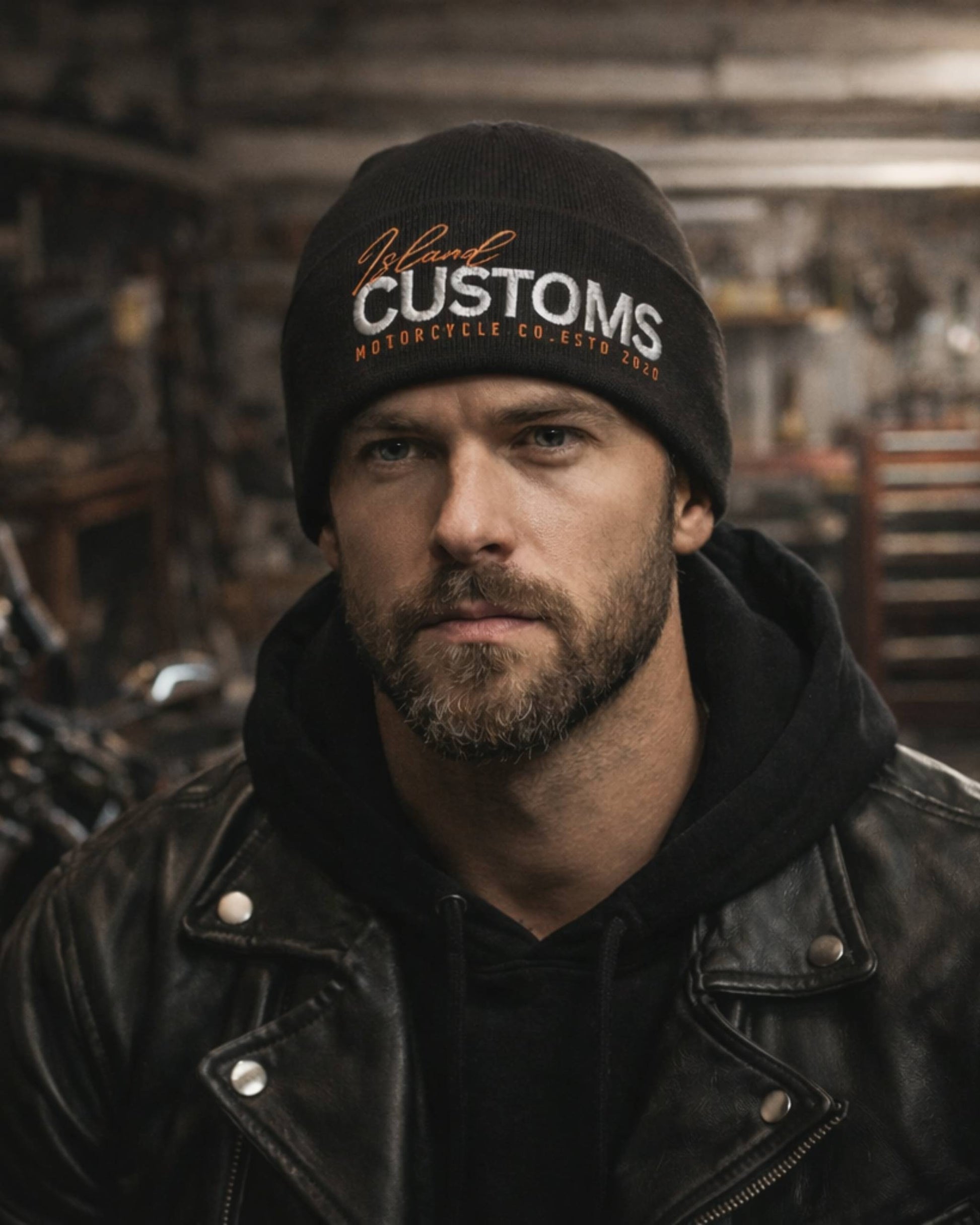 Man wearing a black leather jacket and 'Rural Customs' beanie in a workshop setting