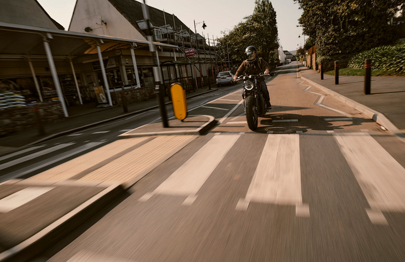 Person riding a motorcycle on a zebra crossing with buildings and trees in the background