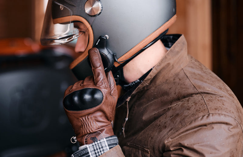Person wearing a dark helmet, brown leather gloves, and a brown jacket.