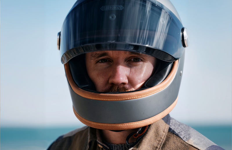 Person wearing a black and brown motorcycle helmet with a clear visor against a blurred background.