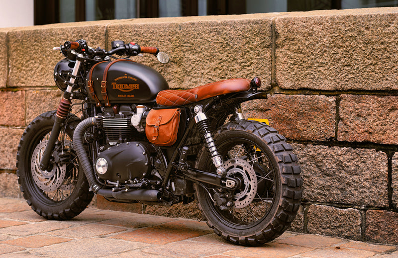 Motorcycle with brown leather seat and saddlebags against a stone wall.