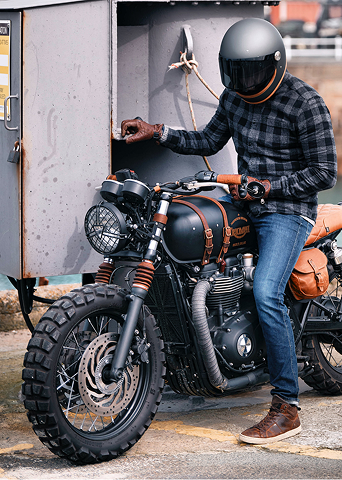 Person wearing a helmet and plaid shirt standing next to a motorcycle by a trailer.