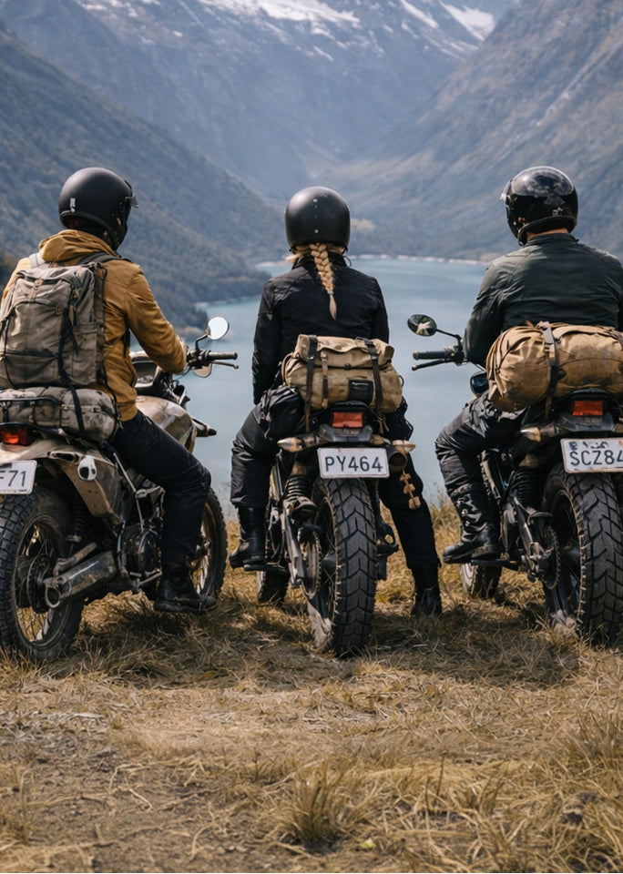 Three people on motorcycles with backpacks, overlooking a scenic mountain landscape.