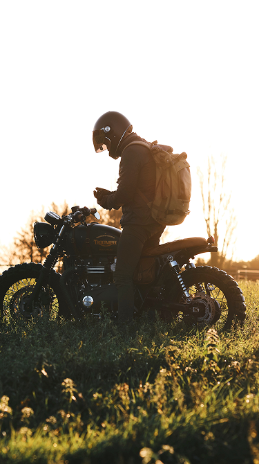 Person sitting on a motorcycle in a field with sunset lighting