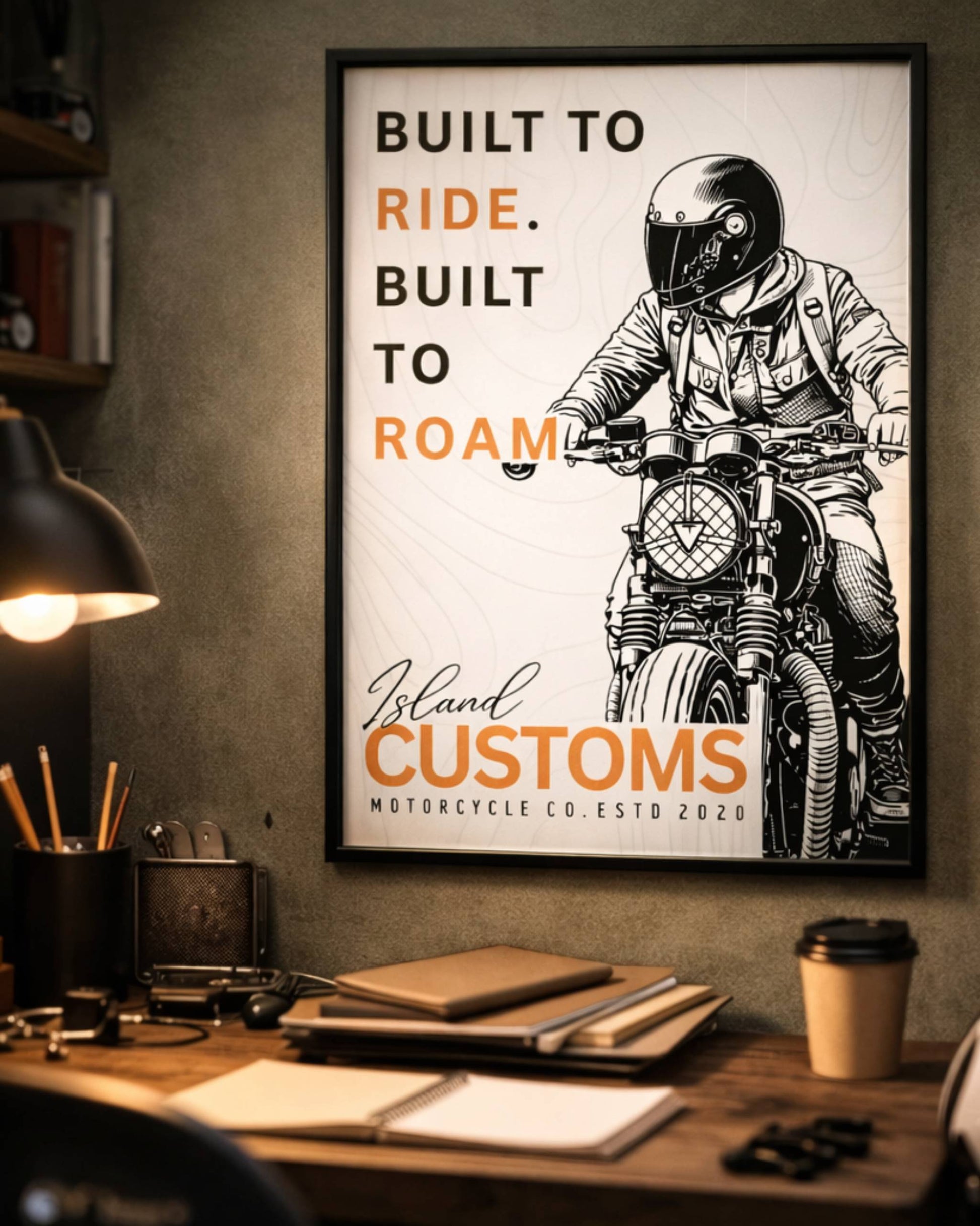 Framed poster with a motorcycle rider and 'Built to Ride, Built to Roam' text on a wall above a desk.