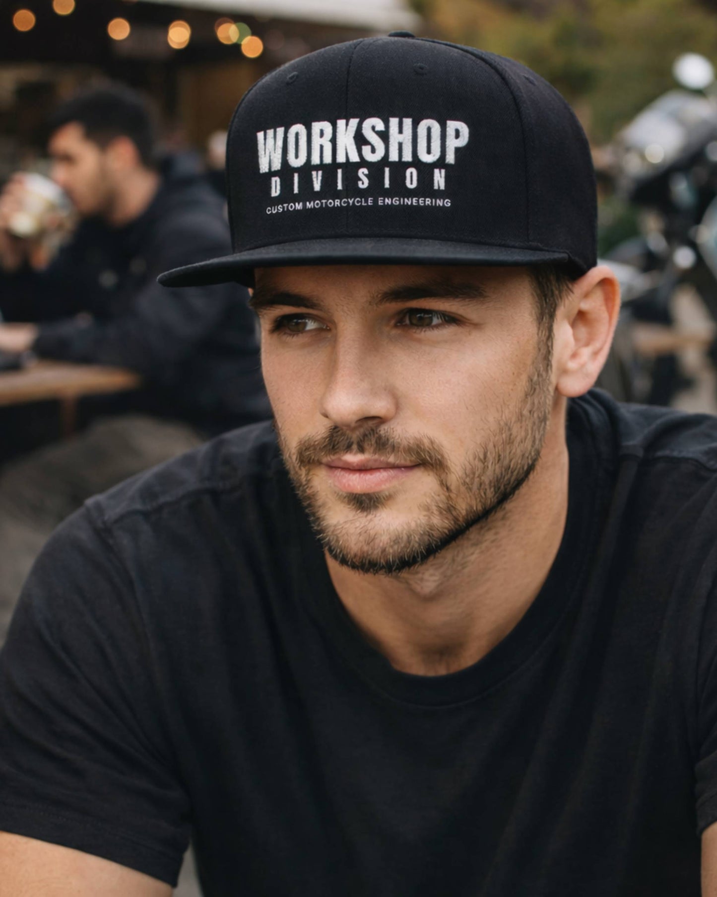 Man wearing a black cap with 'Workshop Division' text, sitting outdoors.