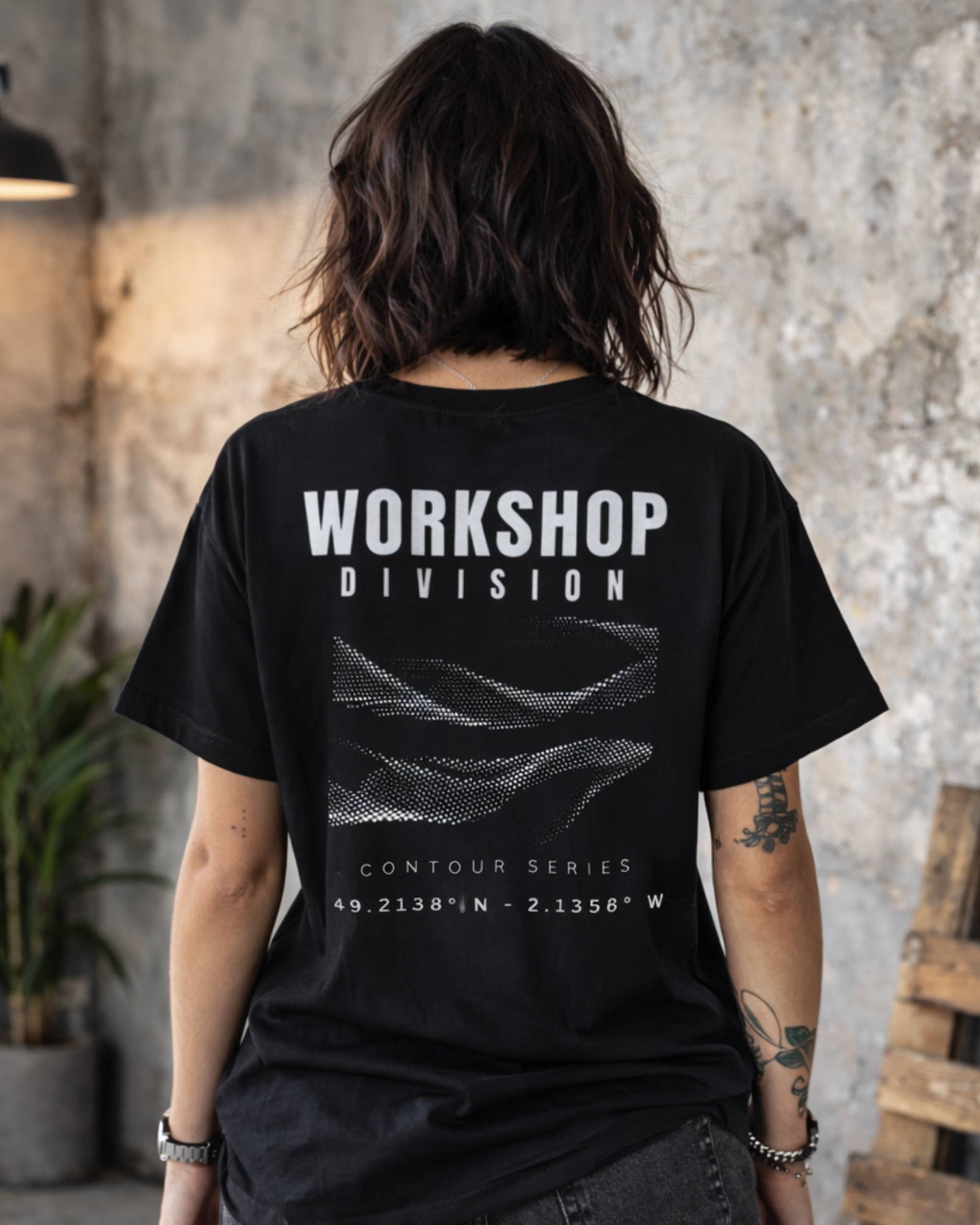 Person wearing a black t-shirt with 'Workshop Division' text on the back, standing in a rustic indoor setting.
