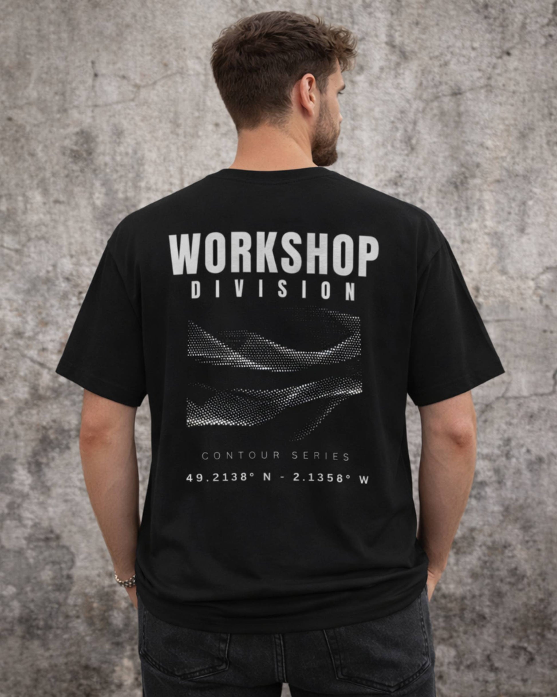 Man wearing a black t-shirt with 'Workshop Division' text on the back against a gray concrete wall.