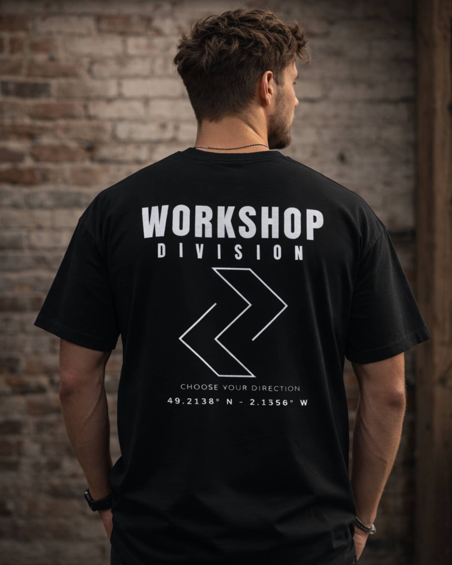 Man wearing a black t-shirt with 'Workshop Division' text and logo against a brick wall.