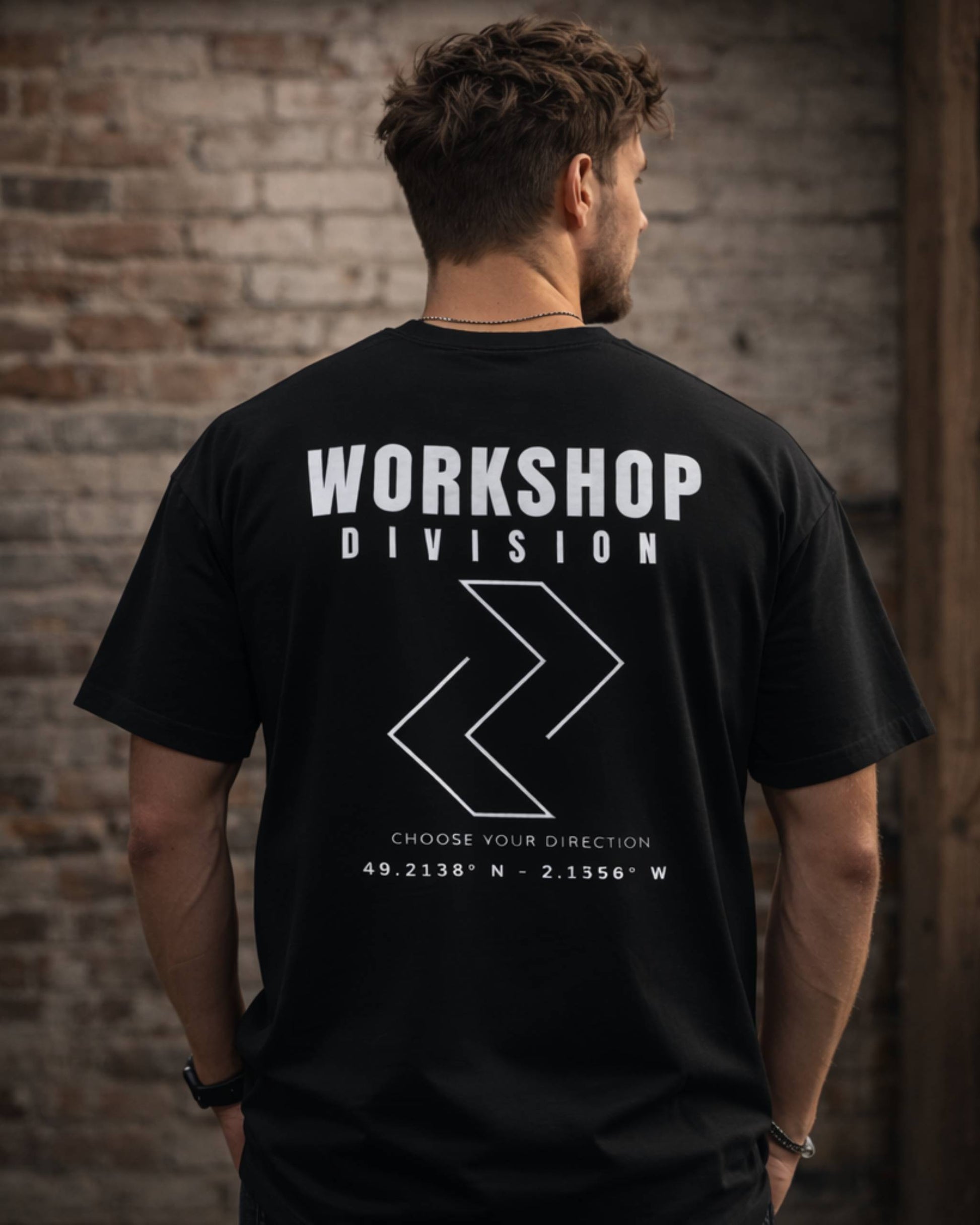 Man wearing a black t-shirt with 'Workshop Division' text and logo against a brick wall.