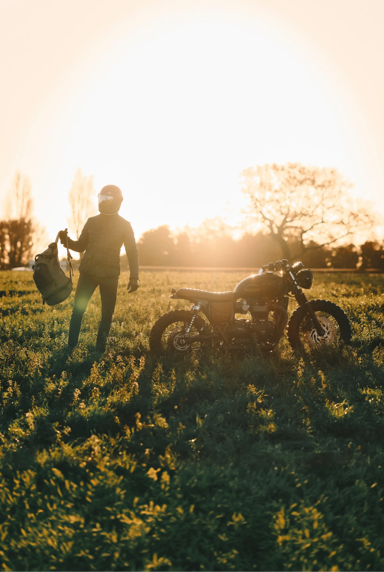 Person standing next to a motorcycle in a field with sunset lighting