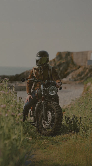 Person on a motorcycle in a scenic outdoor setting with ocean and cliffs.