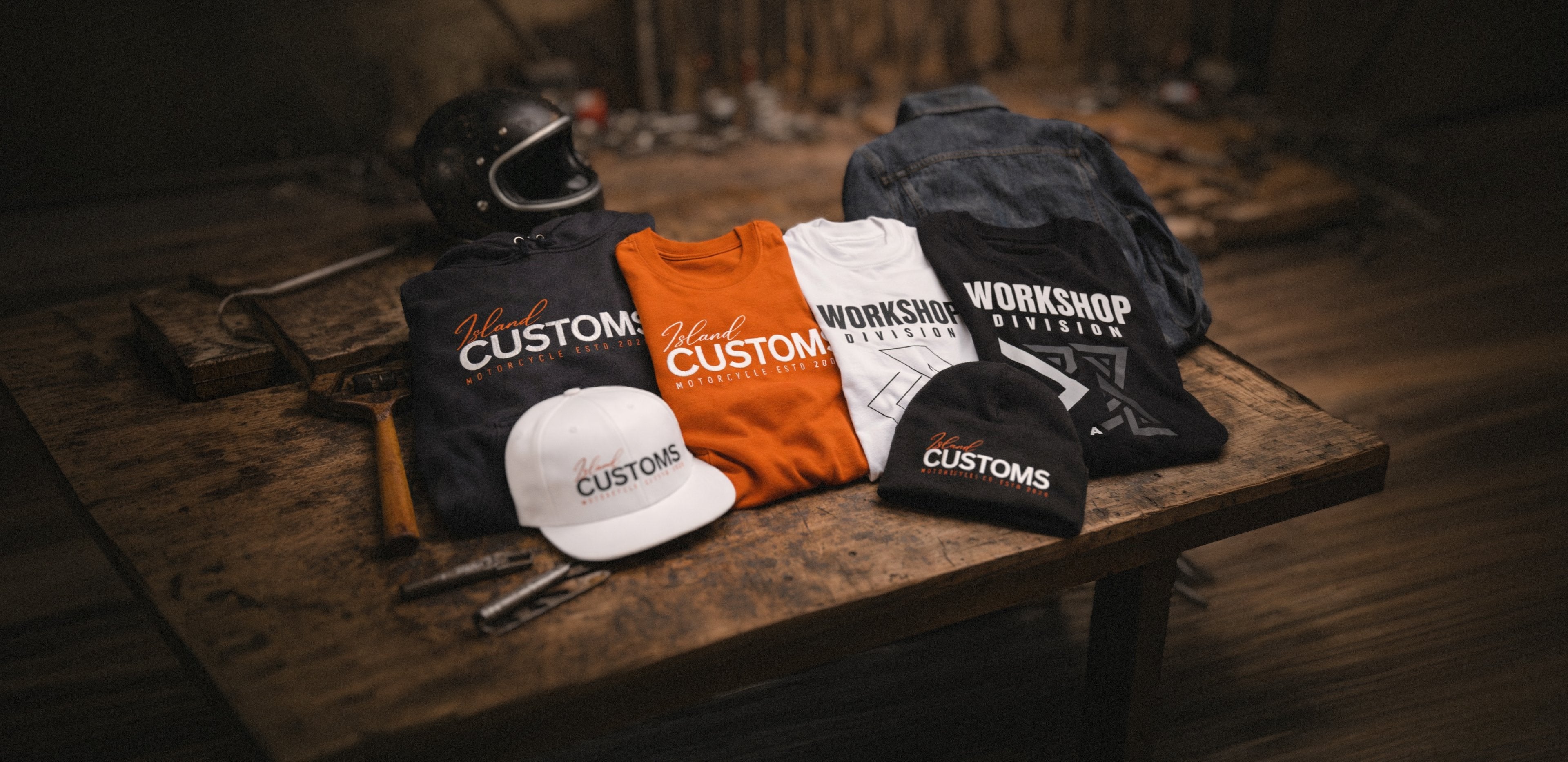 Collection of 'Workshop Customs' branded clothing and helmet on a wooden surface.