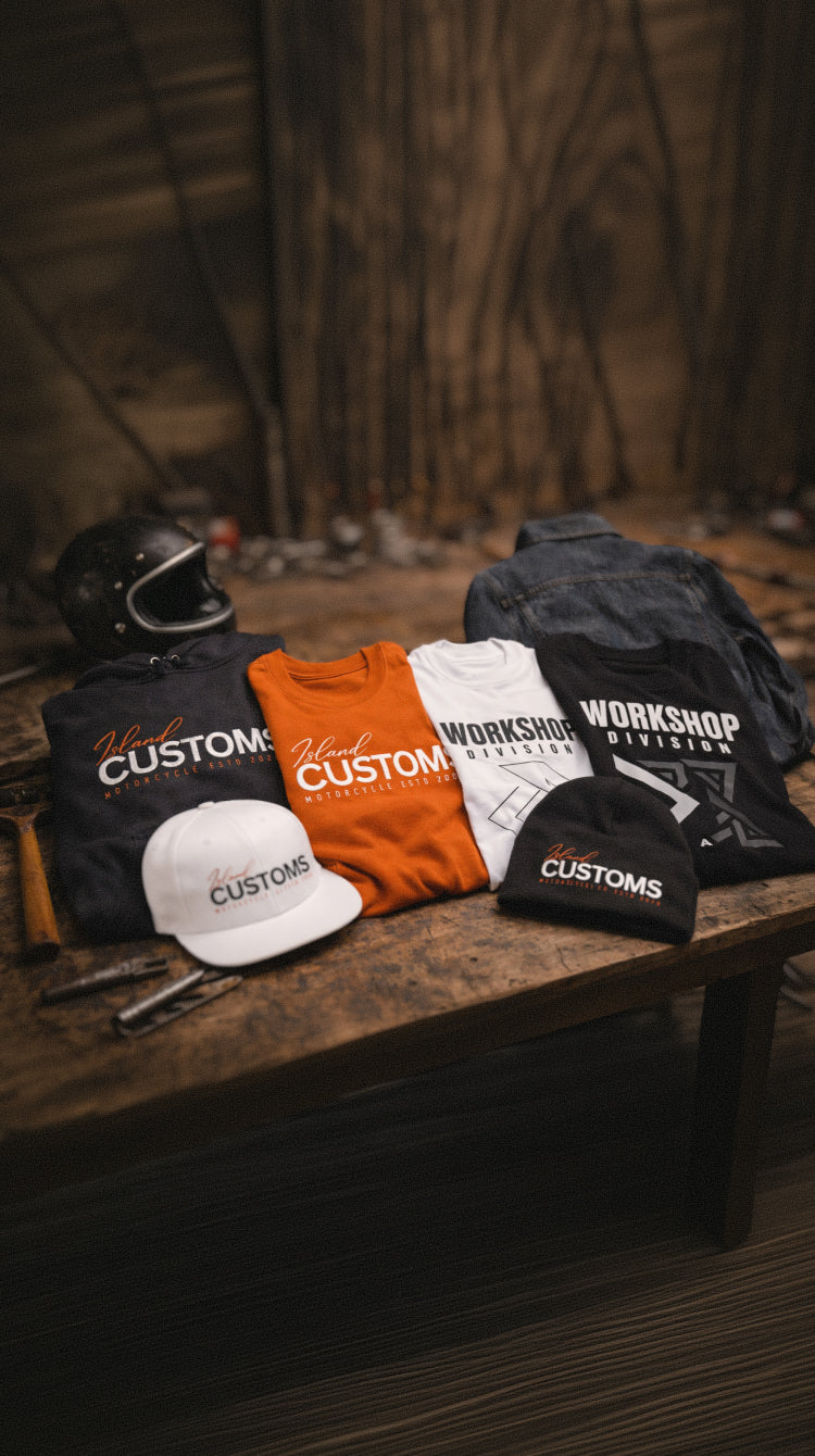 Collection of 'Workshop Customs' branded clothing and accessories on a wooden surface with a rustic background.