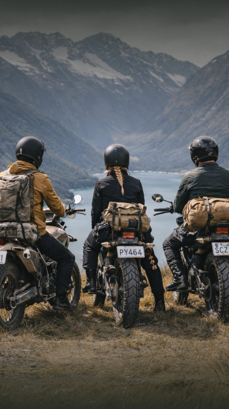 Three people on motorcycles with luggage, looking at a mountain lake.