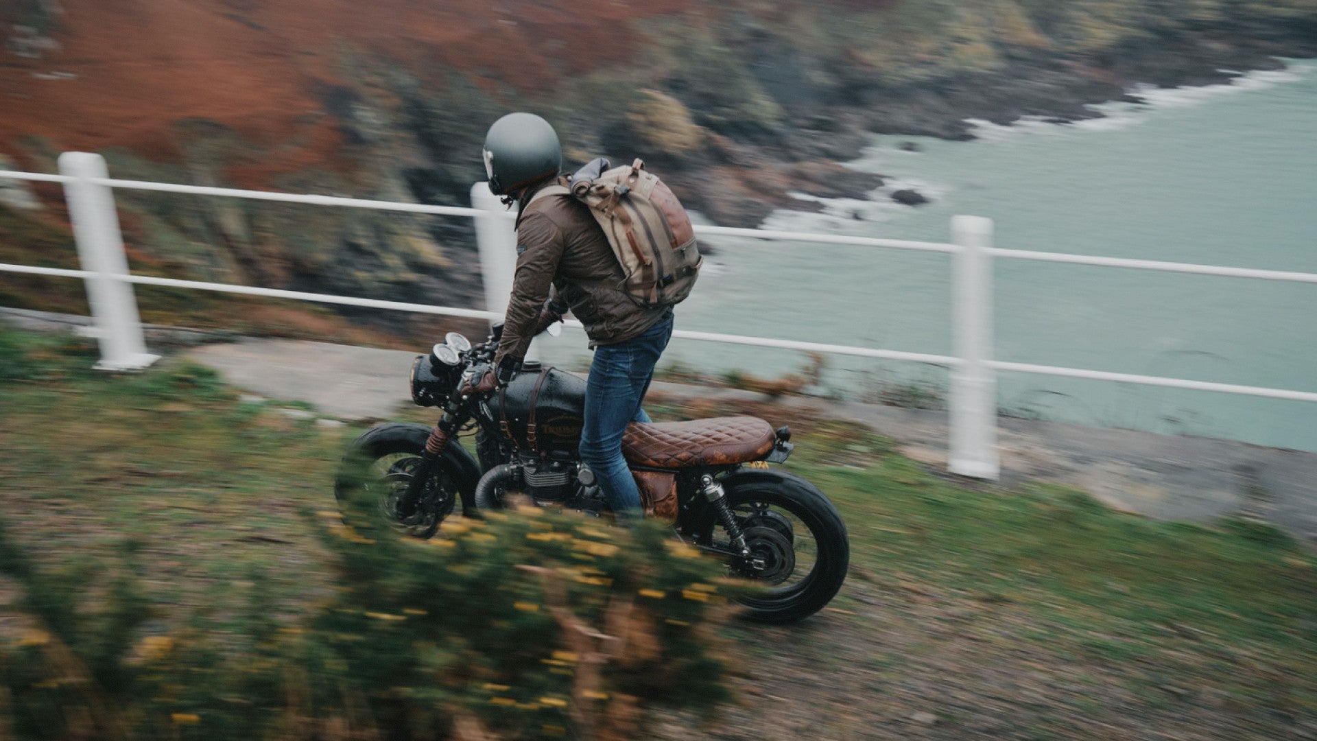Person riding a motorcycle along a coastal road with scenic background