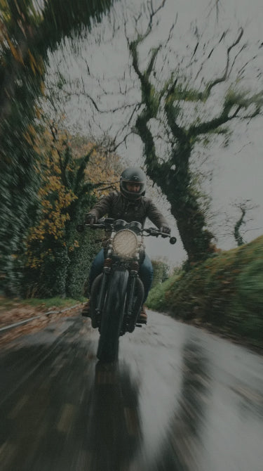 Person riding a motorcycle on a wet road surrounded by trees