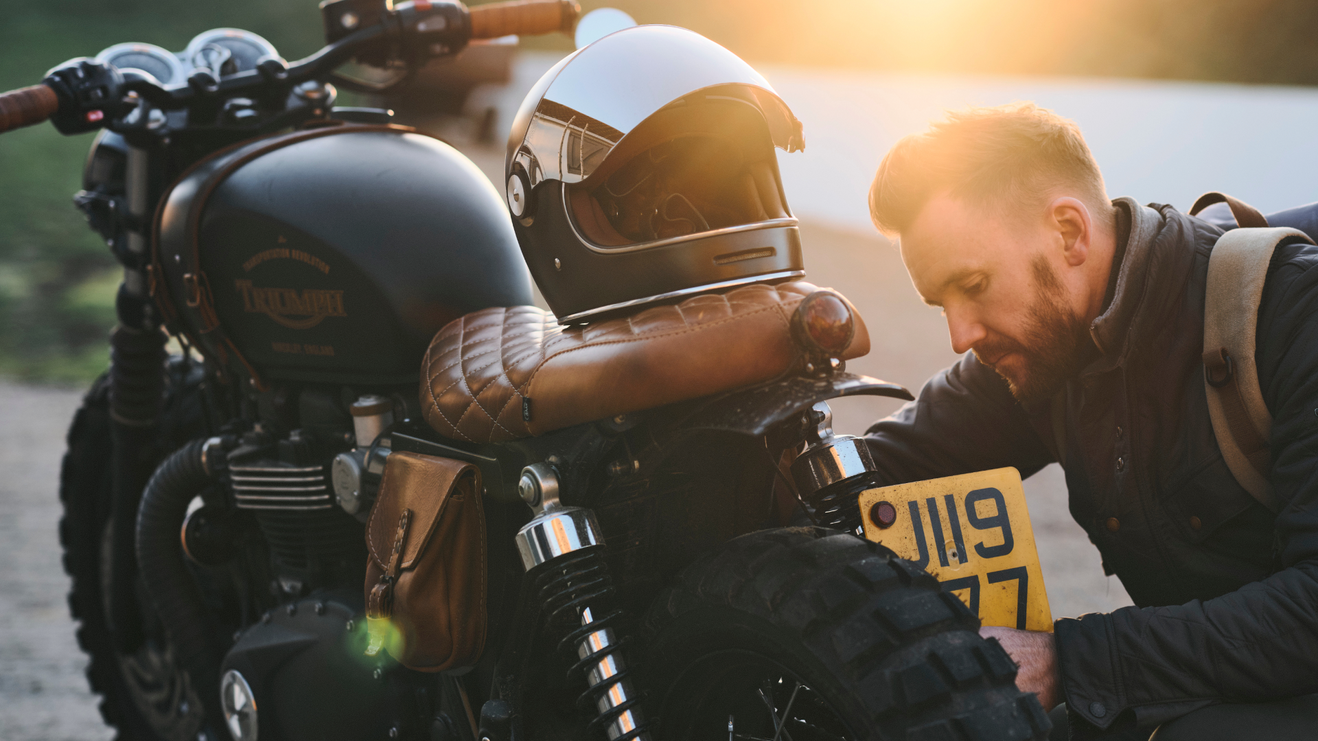Person standing next to a motorcycle in a field at sunset