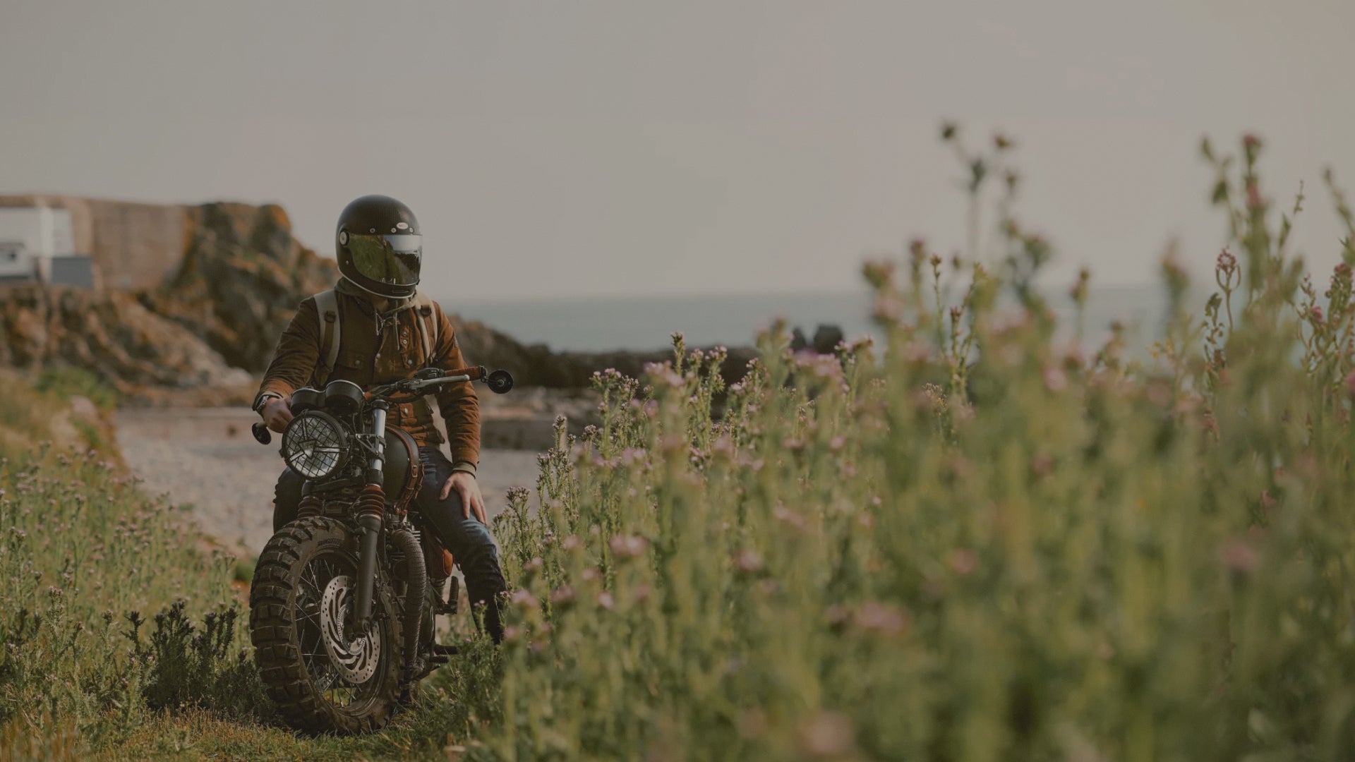 Person riding a motorcycle through a field of tall grass and wildflowers.