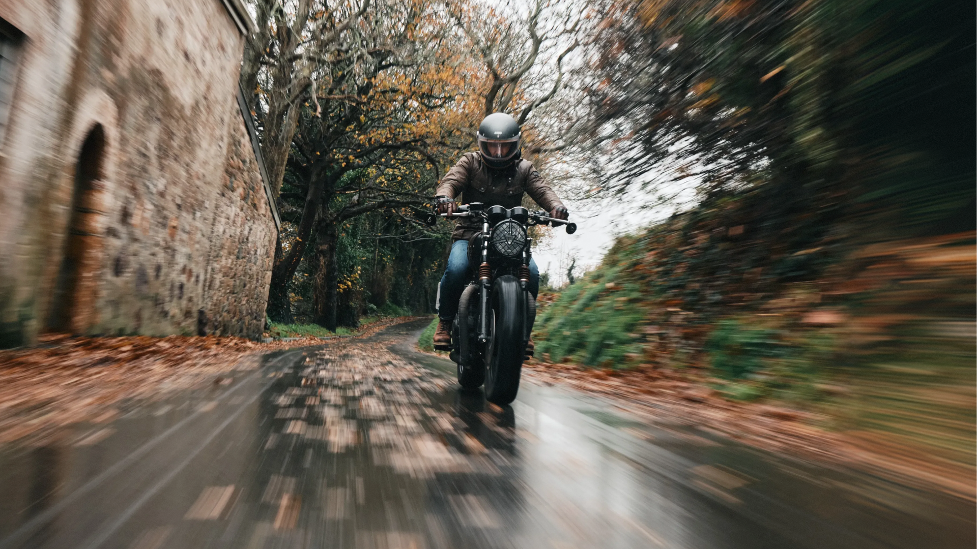 Person riding a motorcycle on a tree-lined road with stone walls.