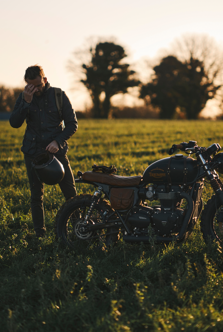 Person standing next to a motorcycle in a field at sunset