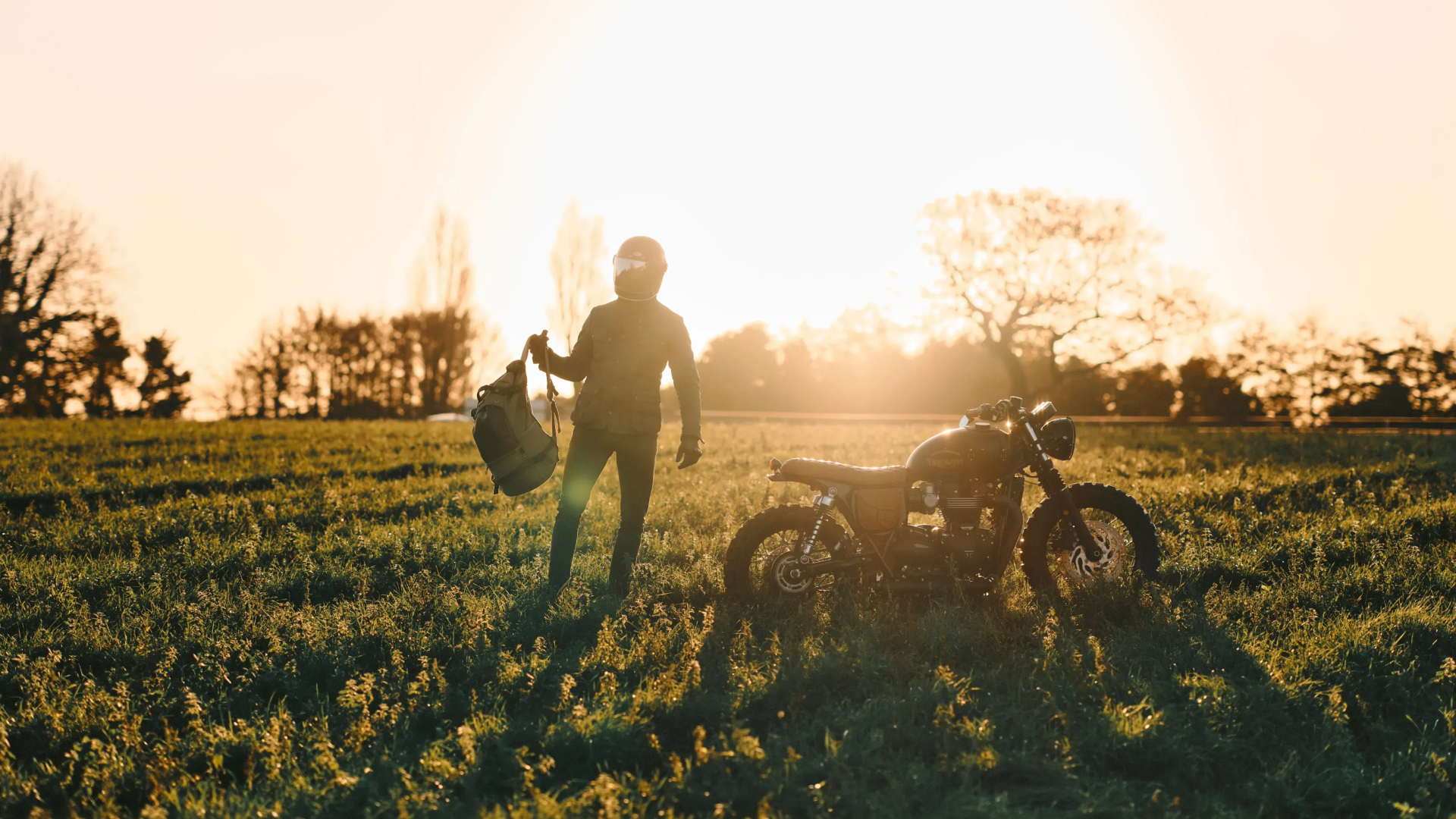 Person standing next to a motorcycle in a field with sunset lighting