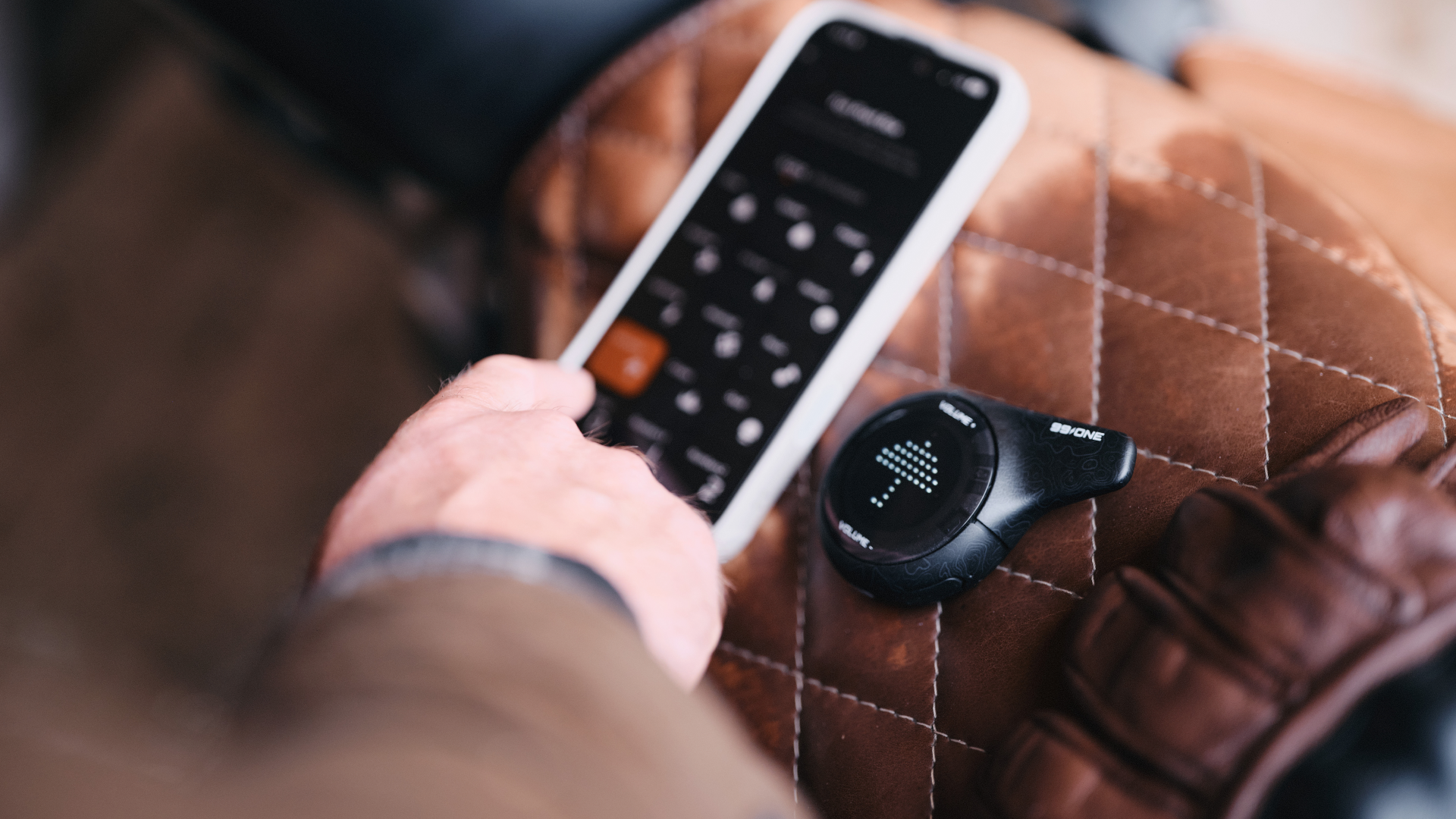 Person holding a smartphone with a remote control app, next to a smartwatch on a brown textured surface.