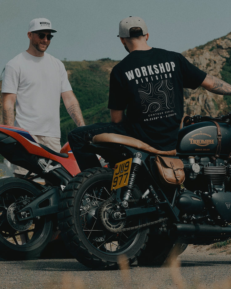 Two men standing next to motorcycles with a mountainous background