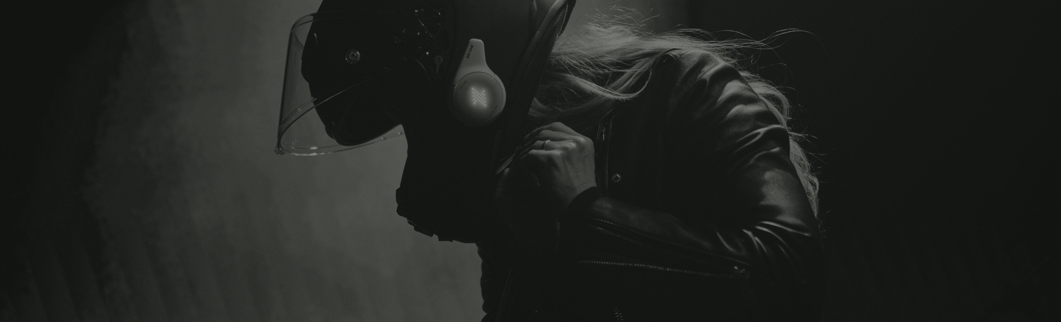 Person wearing a dark hooded outfit with a light source creating a dramatic silhouette effect.