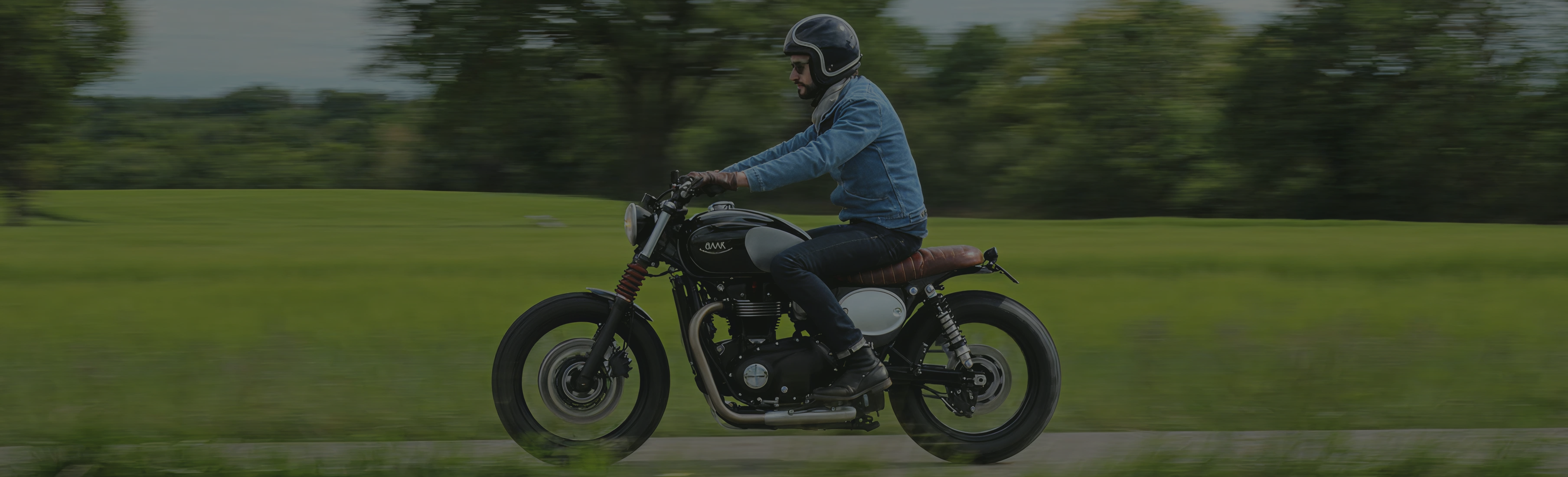 Person riding a motorcycle on a road with greenery in the background