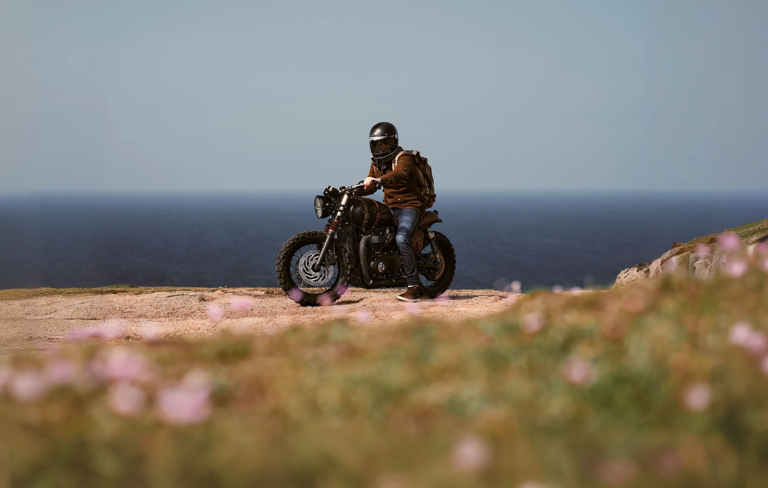 Person on a motorcycle overlooking a scenic landscape with ocean and sky.