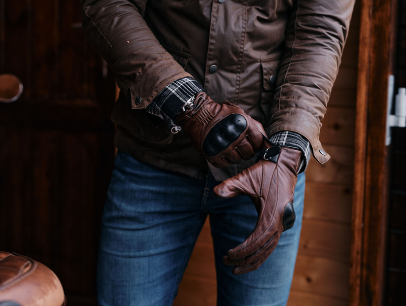 Person wearing brown leather gloves and a jacket in a rustic setting