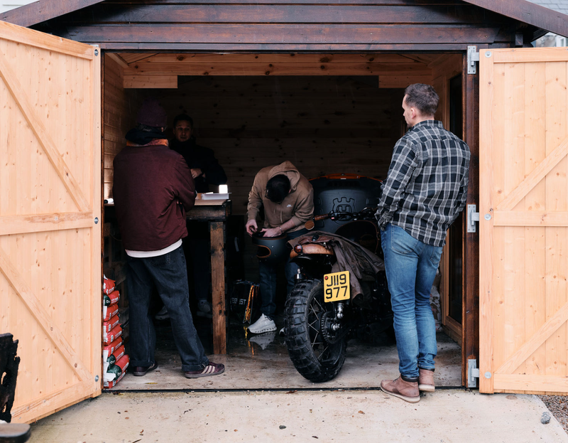 People working on a motorcycle inside a wooden shed