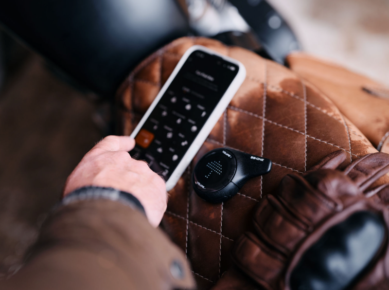 Person holding a smartphone with a remote control app on a brown leather chair.